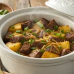 Slow-cooked steak and potato bake in a crockpot topped with melted cheddar cheese and green onions.